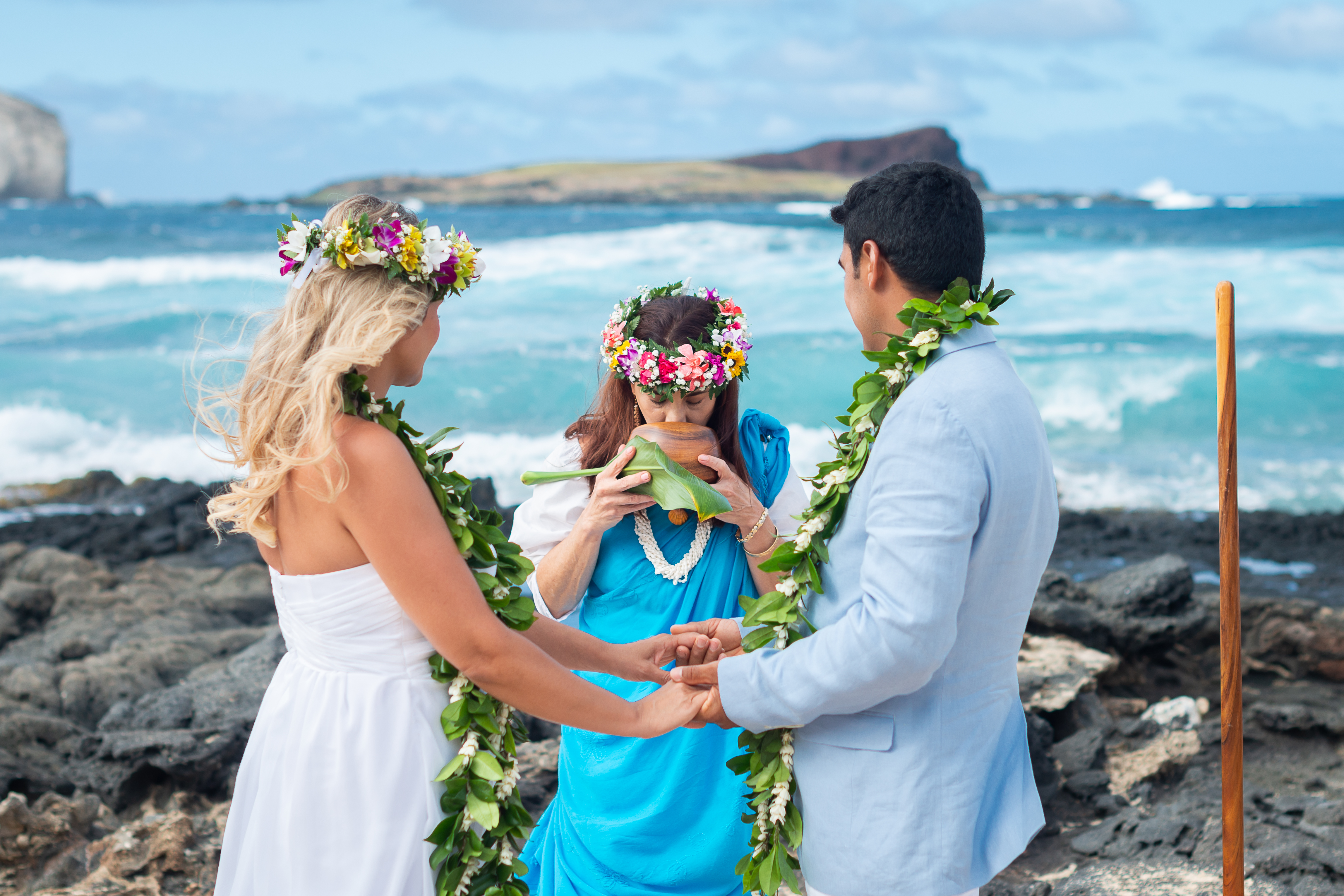 Kahu Pomaikai breathing her HA or breath of life into a wooden bowl in front of a couple
